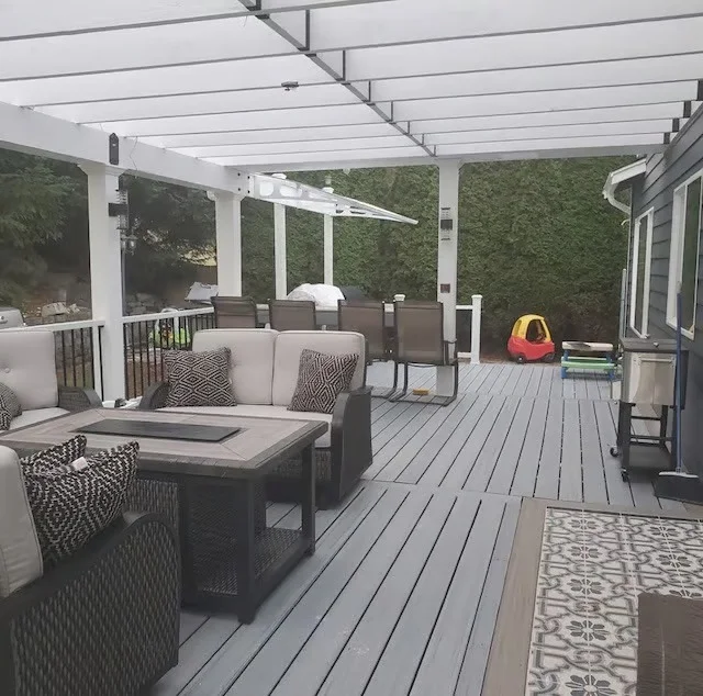 Gray composite deck with white pergola, seating area, fire pit table, and green privacy panels