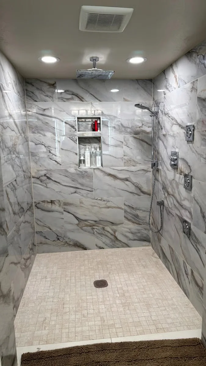 Walk-in shower with marble tile walls, frameless glass door, dual showerheads, and recessed lighting