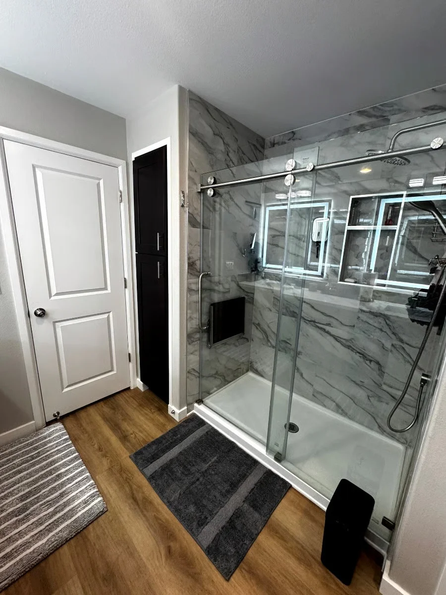 Modern bathroom with marble tile shower, frameless glass doors, and chrome showerhead