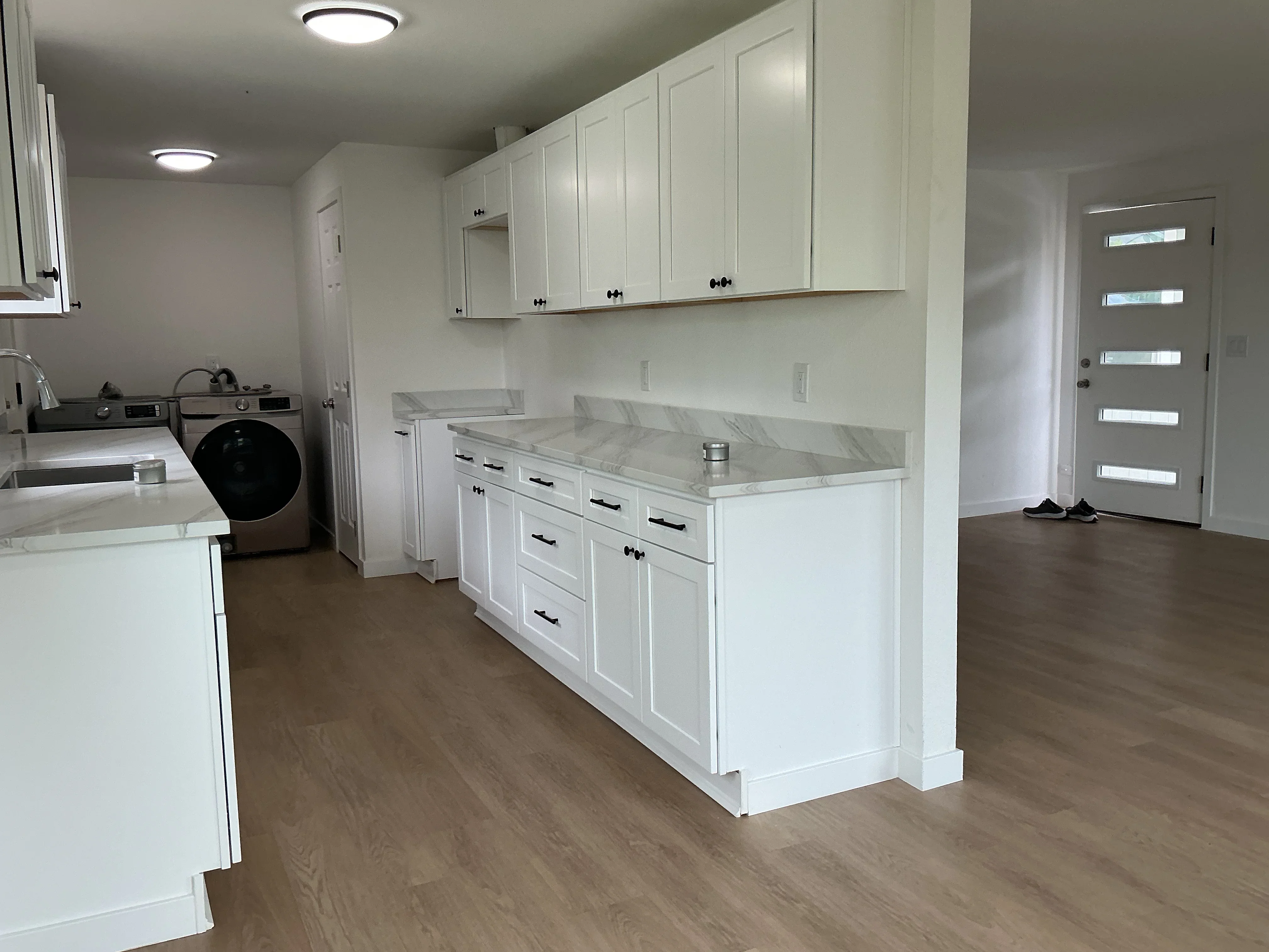 White shaker cabinets with marble countertops, island with waterfall edge, hardwood flooring, modern lighting
